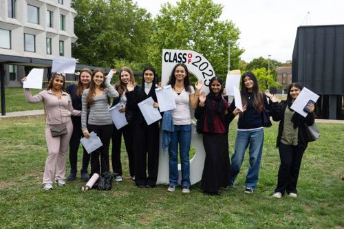 A group of people stand outdoors on a grassy area, holding papers and posing for a photo in front of a large B sign that reads 'CLASS OF 2025'