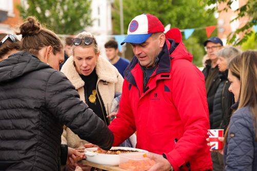 A man wearing a red coat serving food from a large serving dish.