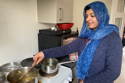 A woman in a blue headscarf stirs a pan of food on the cooker