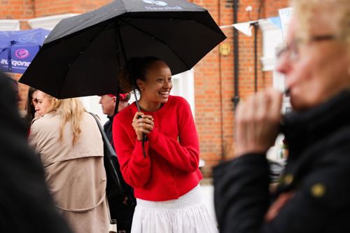 A girl wearing a red cardigan and white skirt holding a black umbrella.