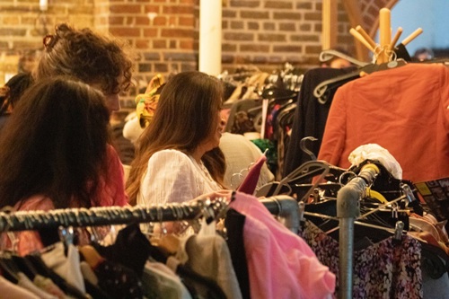 Several women browse rails of clothes as part of a clothes swap event