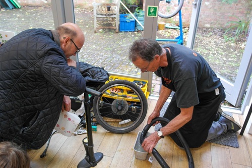 Two men kneel while they mend a bike wheel