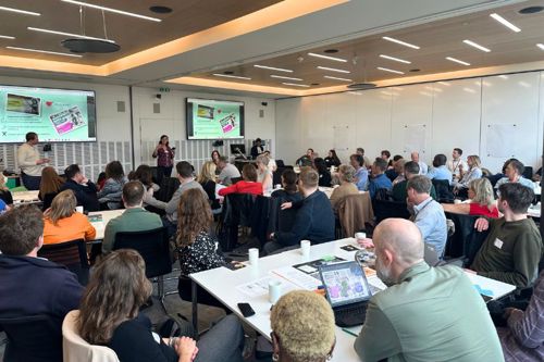 Judi Gasser giving a presentation in front of a room full of people sitting around tables